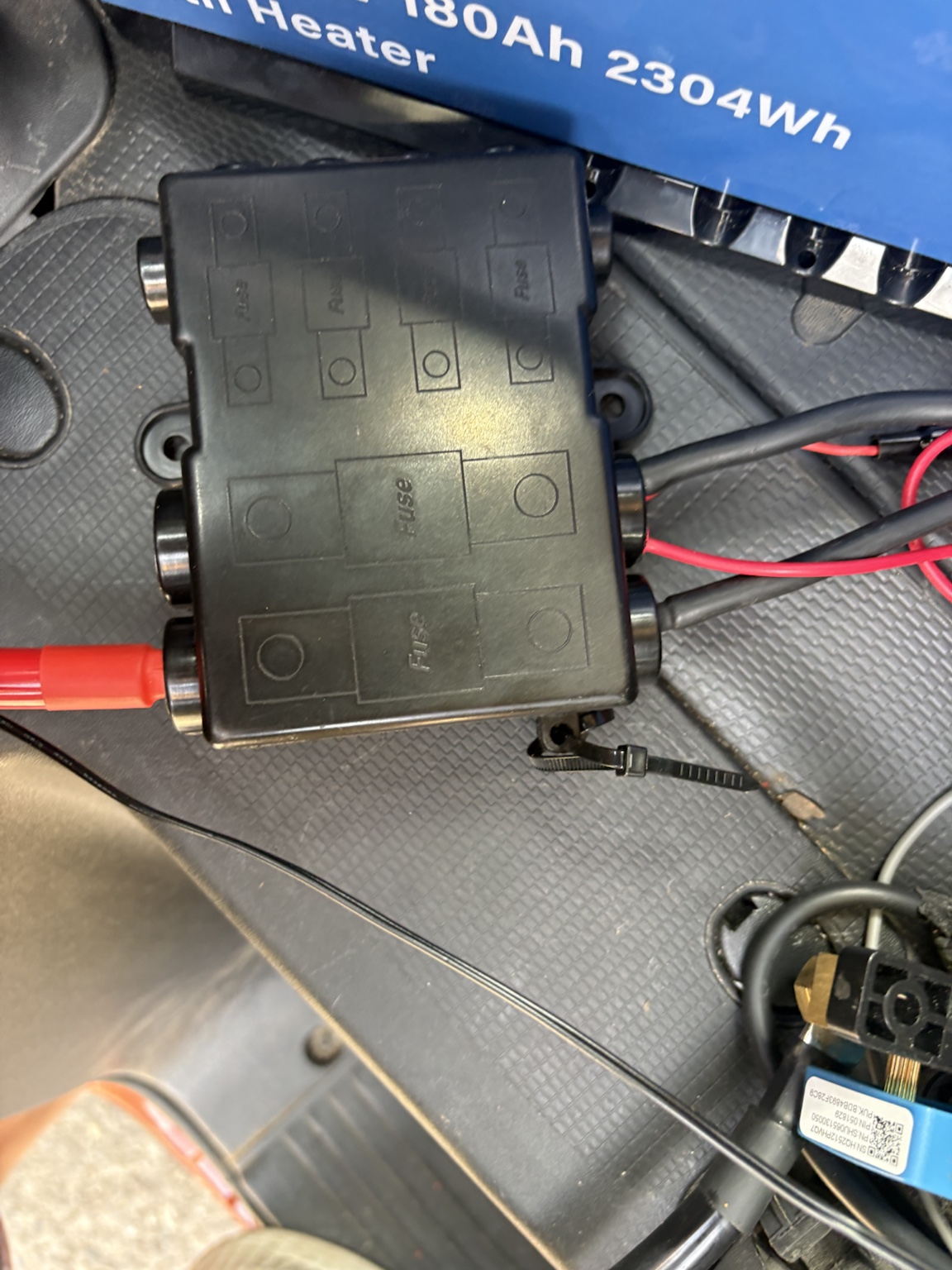 Blaue Ultimatron-180-Ah-LiFePO4-Batterie unter dem Fahrersitz des Clever Celebration. Direkt daneben sitzt der schwarze Sicherungs- und Verteilerhalter; ein kräftiges rotes Pluskabel führt in die Verteilung.