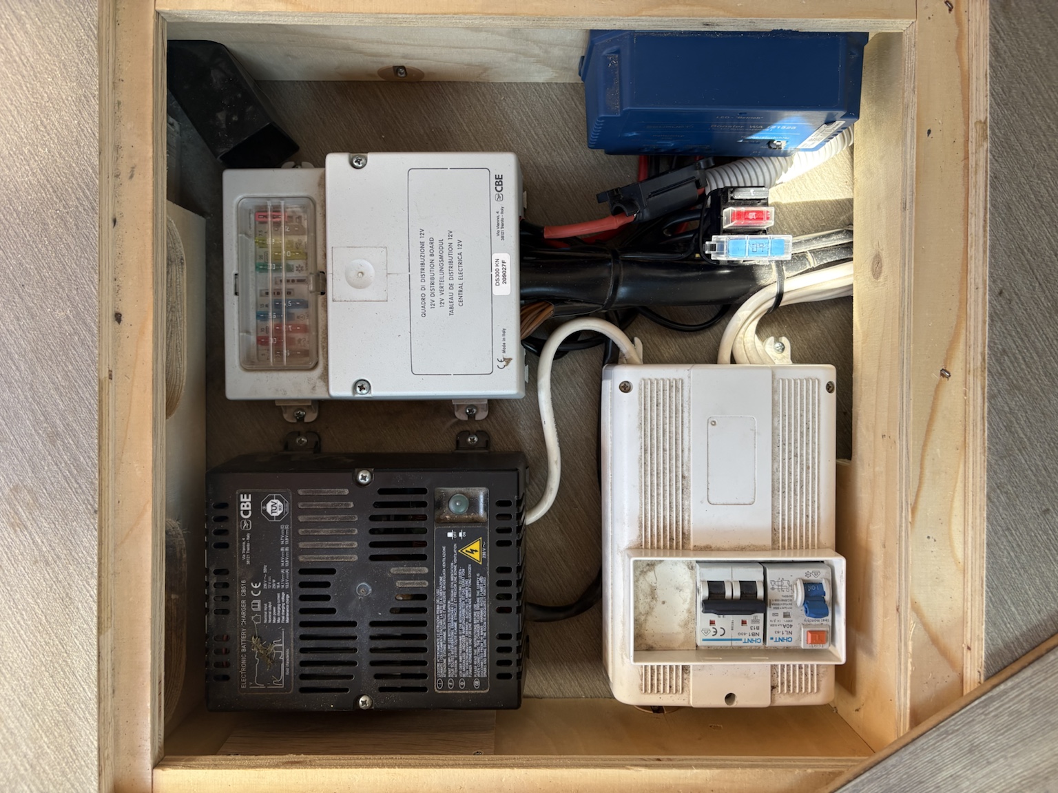 Geöffneter Elektrobereich des Clever Celebration 600 mit CBE-DS300-Verteilung, CBE-Ladegerät, blauem Schaudt-Ladebooster, Sicherungen und dicht verlegten 12-Volt-Kabeln.